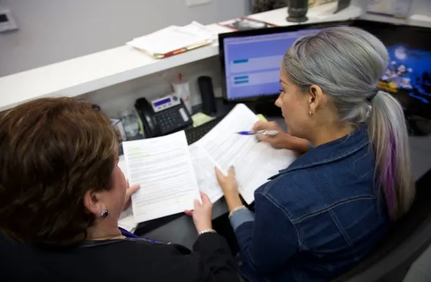 A dental administrator coaching a team member through paperwork at the front desk